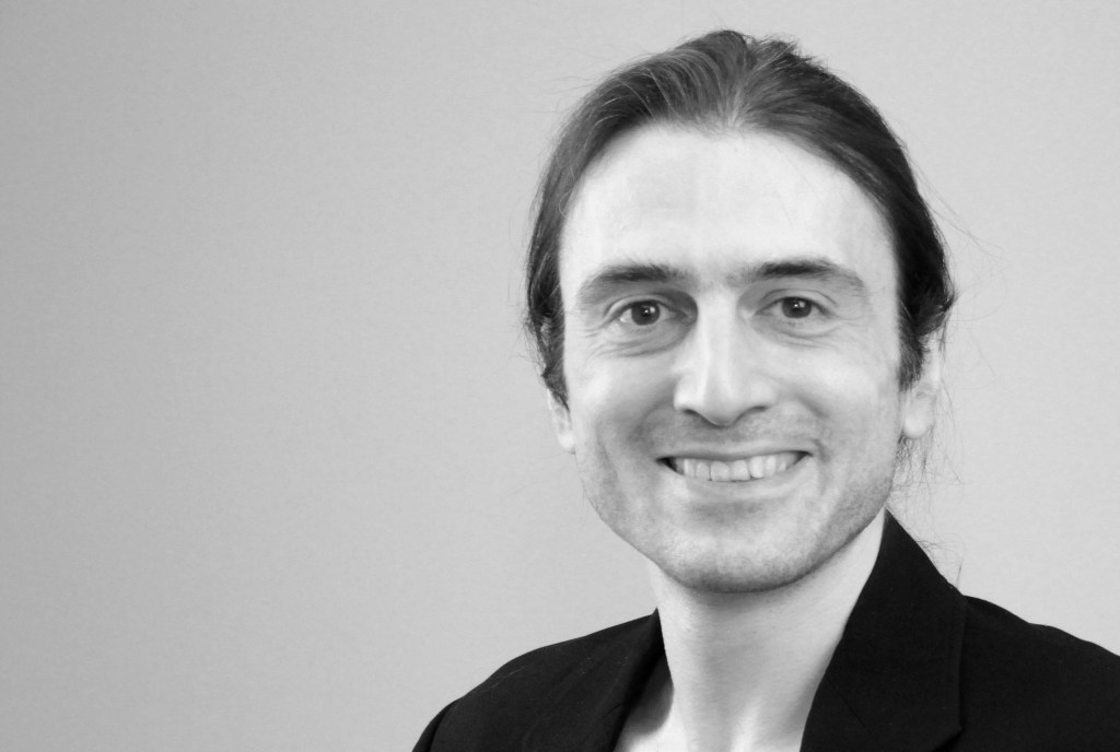 Portraitfoto von Nils Mille in schwarzweiß mit lanen Haaren und schwarzem Hemd